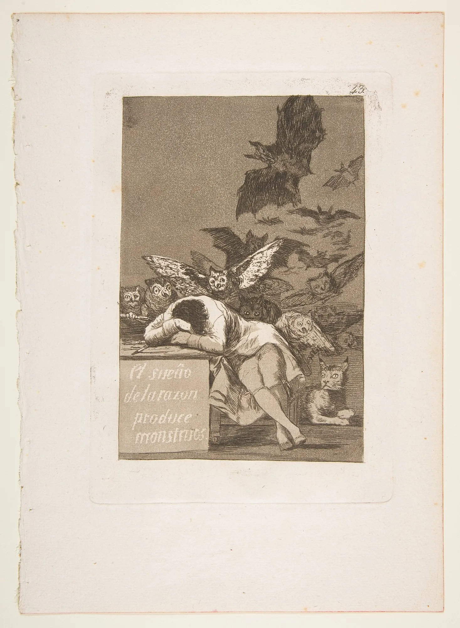 Goya's etching of a man asleep with his head on a desk while owls and bats rise out of the darkness behind him and a cat crouches at his feet.