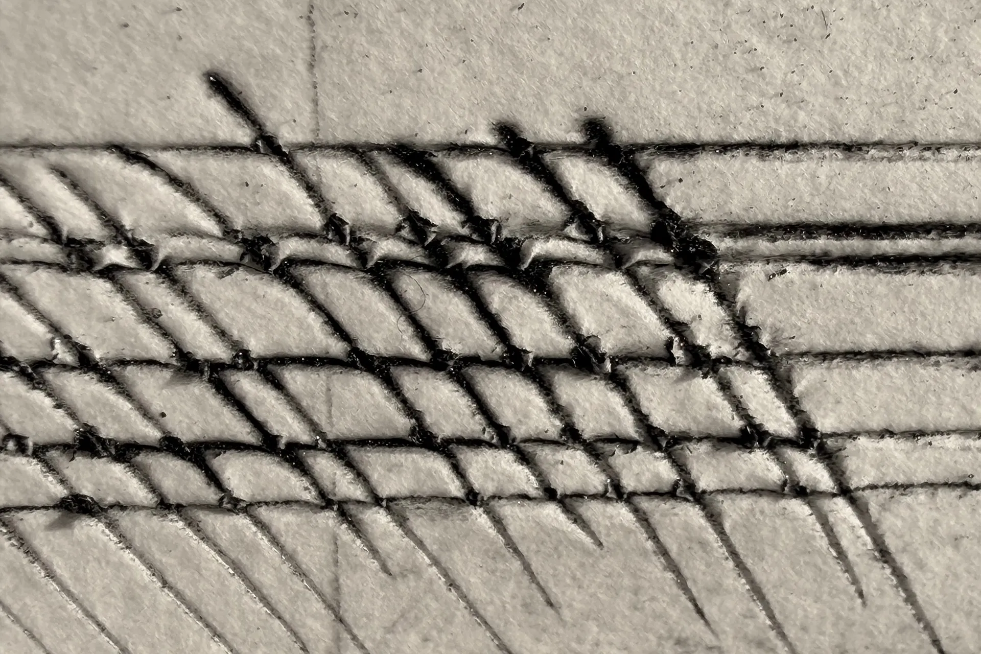 Close detail of a cardboard drypoint test plate by Jenny Robinson, the surface lifted and torn where cross-hatched lines meet.