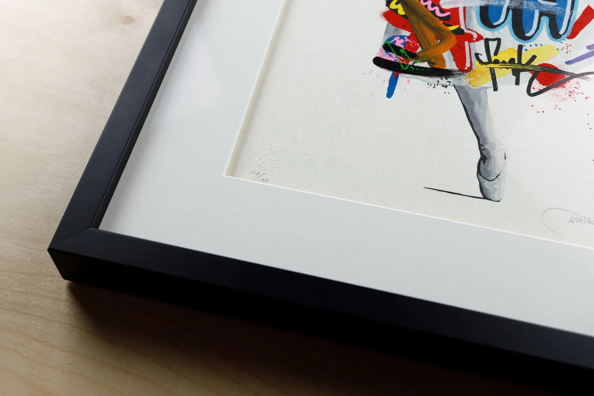 The framed corner of a vivid graffiti-style print, its pencil edition number "112/150" visible in the white margin.