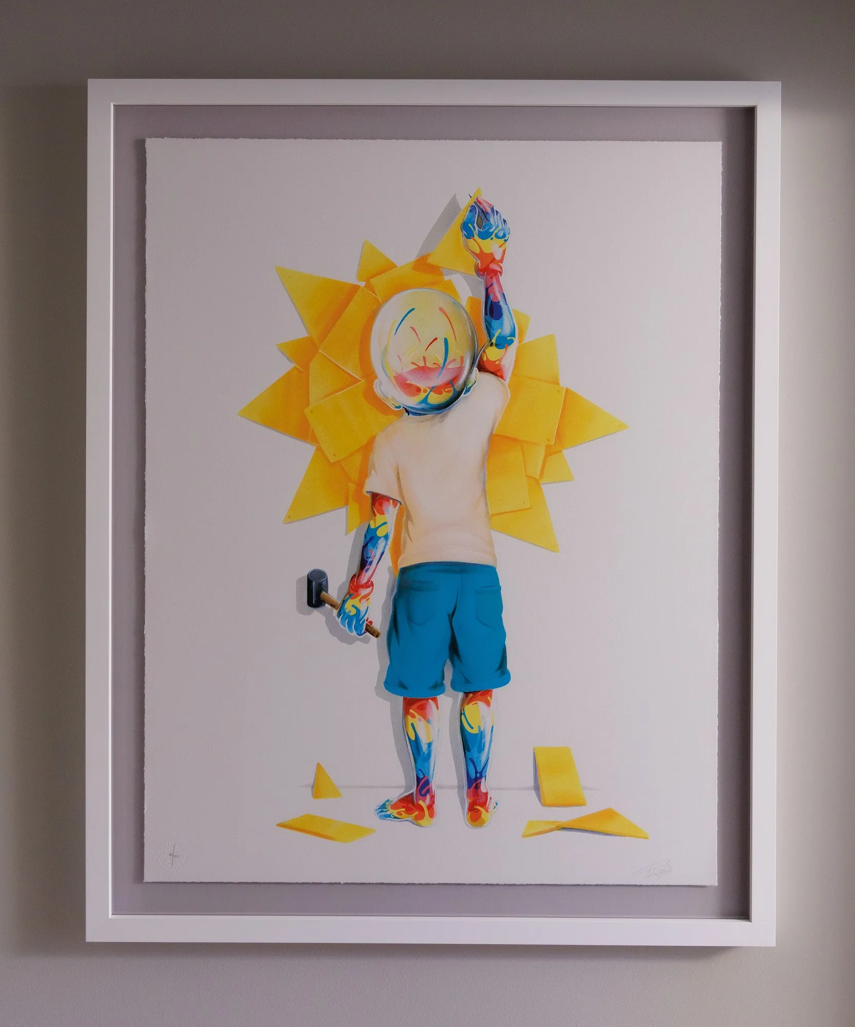 FLOG's Sunrise, framed in white and floated on light grey: a small figure seen from behind, with a glass head and colour-marbled arms and legs, holds a mallet and fixes yellow shards of a sun to the wall, with more pieces lying at his feet.