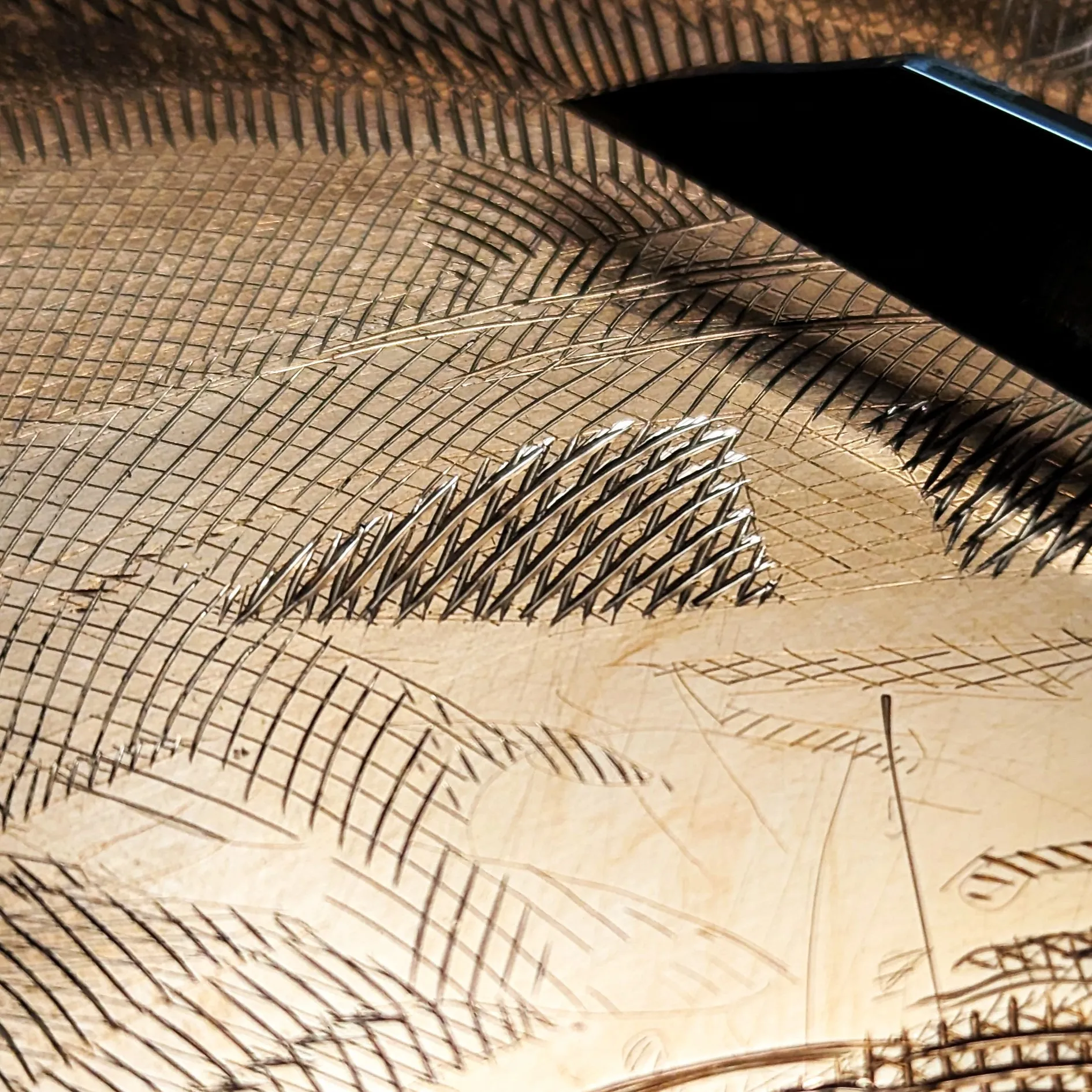 Close-up of a burin’s steel tip resting on a copper plate covered in fine cross-hatched lines, some dark and some catching the light.
