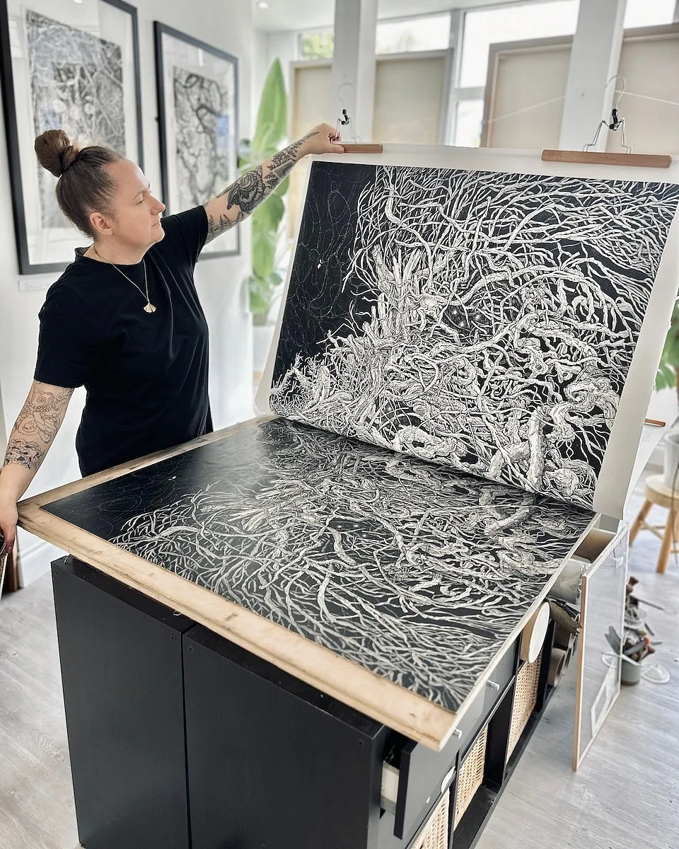 A large printed sheet of Habitat raised on hanging battens, with the carved lino block lying on the surface beneath it.